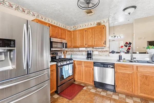 a kitchen with stainless steel appliances granite countertop a stove a sink dishwasher and a refrigerator with wooden cabinets