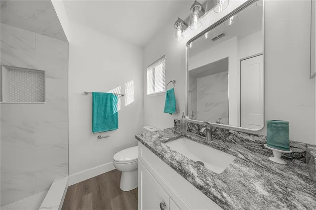 a spacious bathroom with a granite countertop sink a toilet a mirror and shower