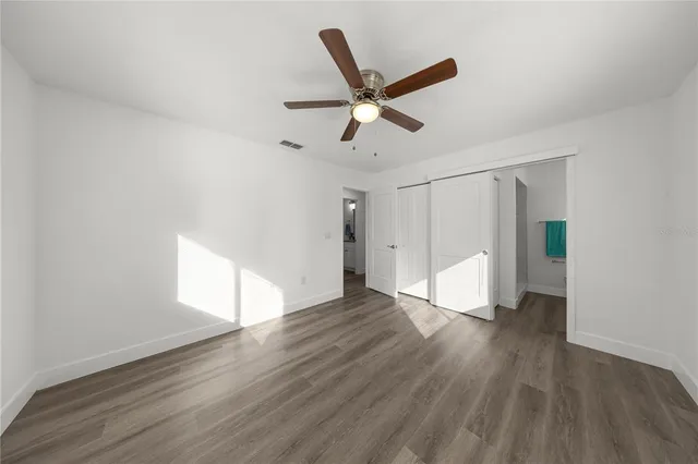a view of an empty room with wooden floor and a ceiling fan