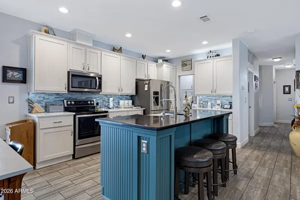 a kitchen with stainless steel appliances kitchen island granite countertop a stove top oven a sink dishwasher a refrigerator and a dining table with wooden floor