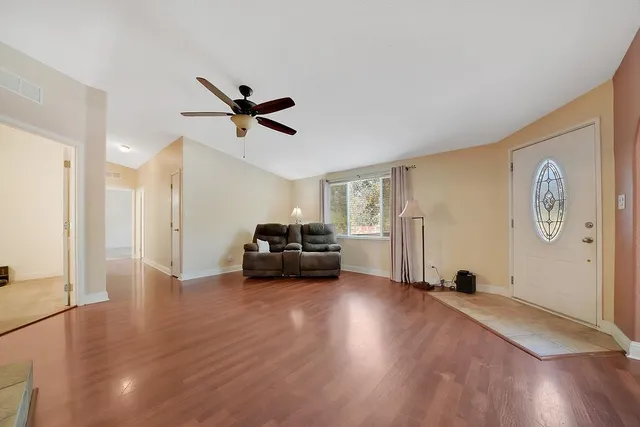 a view of a livingroom with wooden floor a ceiling fan a fireplace and windows
