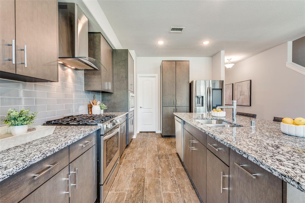 1240 Morning Ridge Trail Aubrey, TX 76227 - Photo 8 of 25 Kitchen featuring appliances with stainless steel finishes, light stone countertops, wall chimney exhaust hood, tasteful backsplash, and modern cabinets