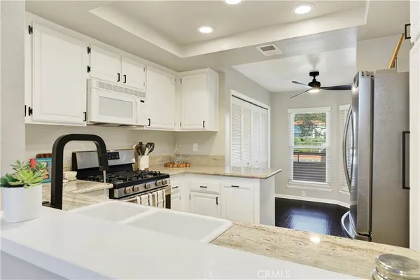 a kitchen with stainless steel appliances granite countertop a stove a sink dishwasher and white cabinets with wooden floor