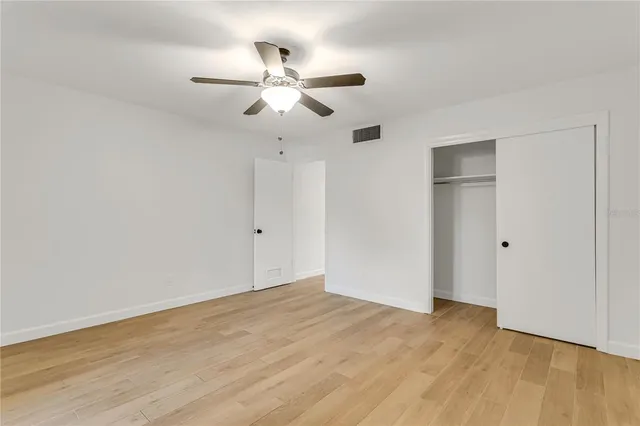 an empty room with wooden floor fan and windows