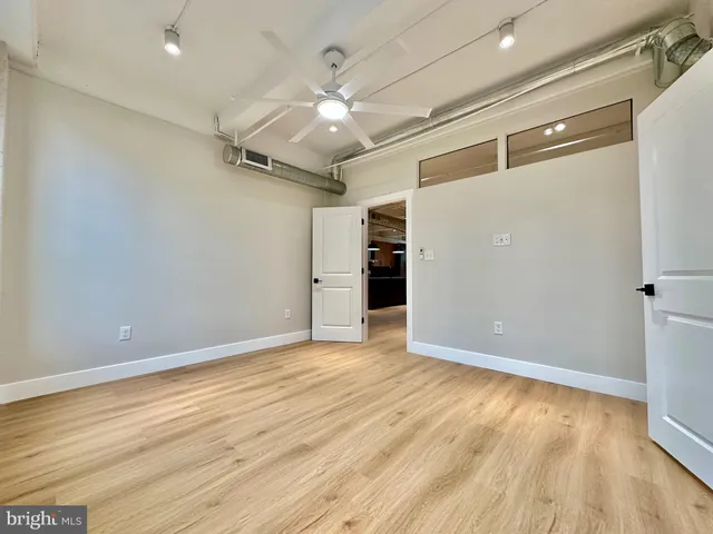 a view of an empty room with wooden floor and a ceiling fan