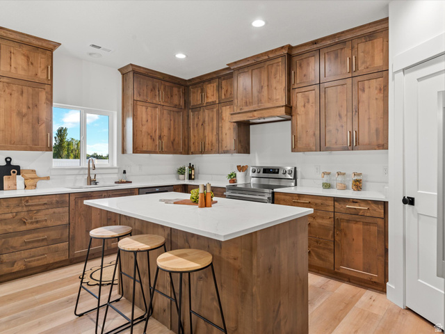 1267 West 2350 South Perry, UT 84302 - Photo 19 of 35 Gourmet kitchen featuring a central island with a solid surface countertop, extensive wood cabinetry, wood-finish flooring, recessed lighting, and a stainless steel range