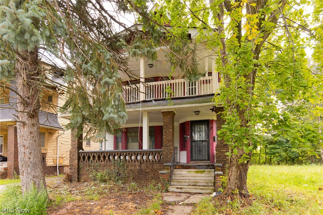1069 Carlyon Road East Cleveland, OH 44112 - Photo 2 of 25 Two-story facade with a covered entry, upper-level balcony, brick columns, and a decorative brick porch railing