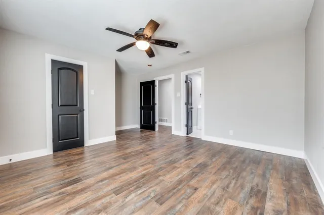 a view of an empty room with wooden floor and a ceiling fan