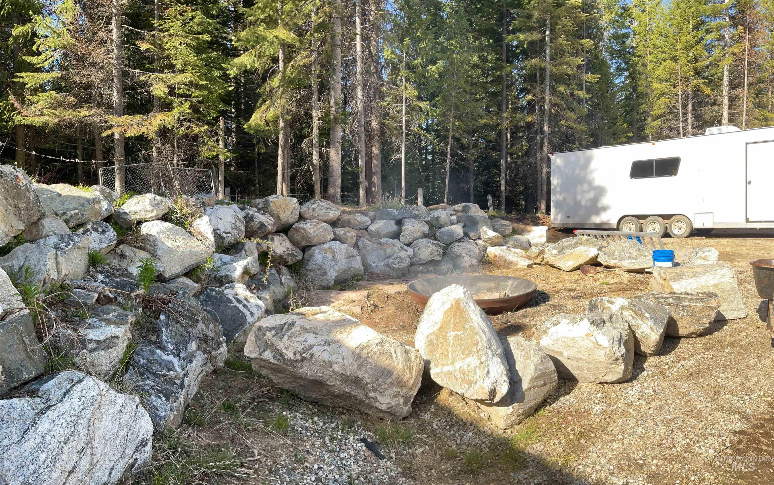 176 West Buffalo Gulch Road Elk City, ID 83525 - Photo 28 of 38 Rock retaining wall bordering a wooded area, featuring a fire pit with surrounding boulder seating