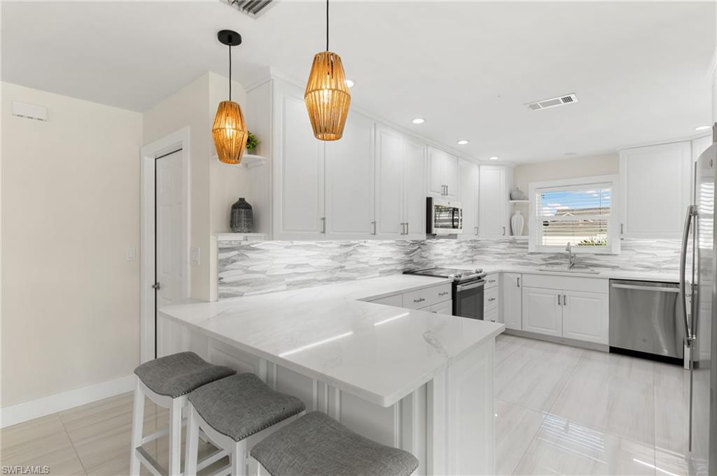 321 Columbus Way Marco Island, FL 34145 - Photo 12 of 40 Kitchen with open shelves, a peninsula, white cabinetry, a breakfast bar, and appliances with stainless steel finishes