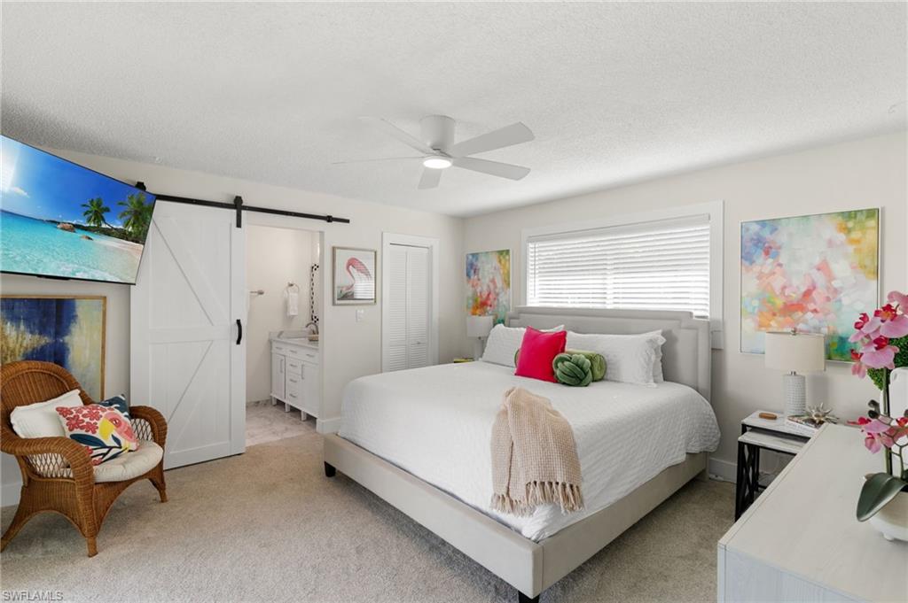 321 Columbus Way Marco Island, FL 34145 - Photo 17 of 40 Bedroom with a barn door, connected bathroom, light colored carpet, a ceiling fan, and a textured ceiling