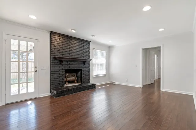 a view of an empty room with wooden floor fireplace and a window