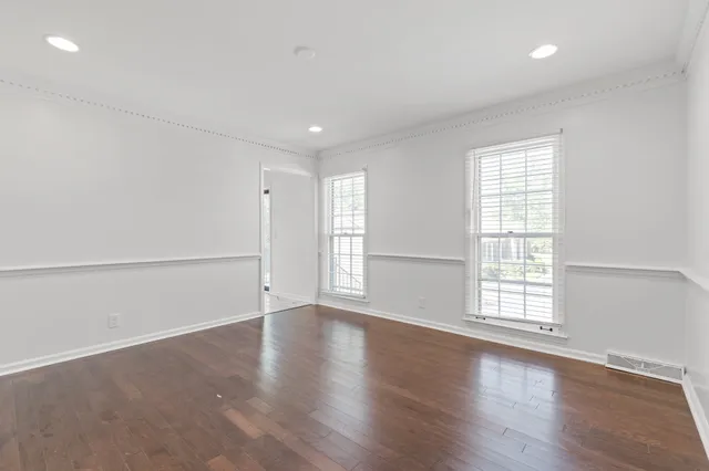 an empty room with wooden floor and windows with curtains