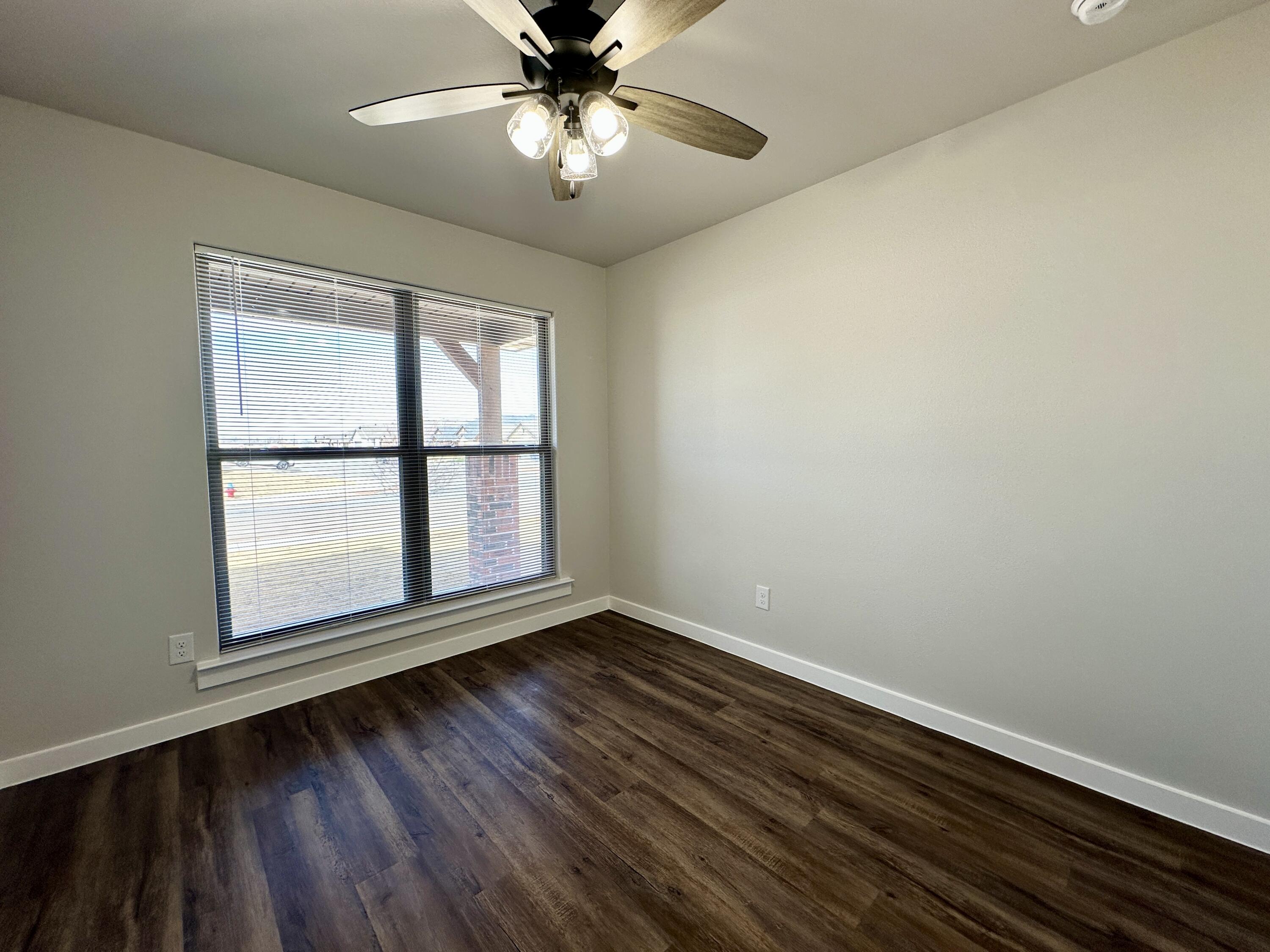 7449 28th Street Lubbock, TX 79407 - Photo 10 of 11 an empty room with wooden floor chandelier fan and windows