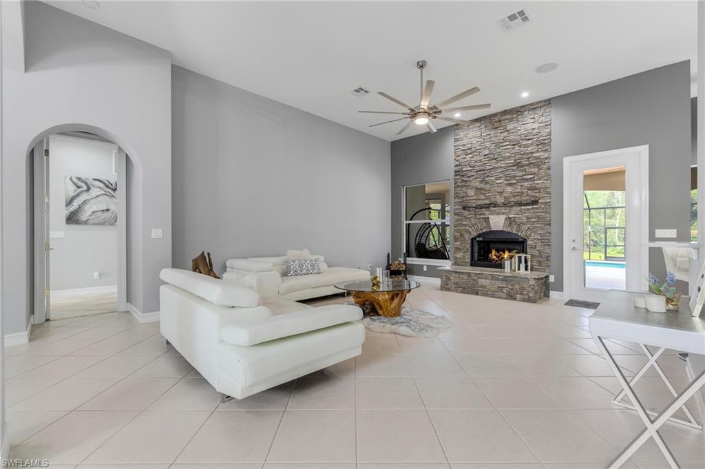 160 Logan Boulevard South Naples, FL 34119 - Photo 3 of 49 Living area featuring a stone fireplace, light tile patterned flooring, arched walkways, and a ceiling fan
