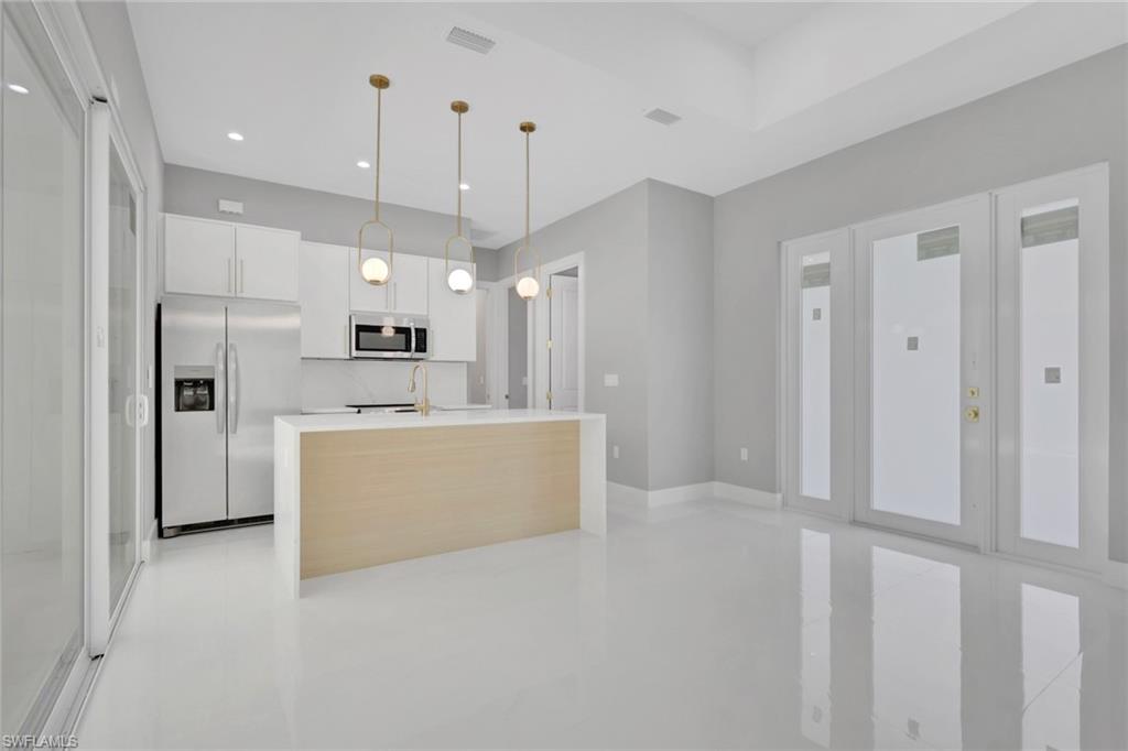 160 Logan Boulevard South Naples, FL 34119 - Photo 34 of 49 Kitchen with white cabinetry, appliances with stainless steel finishes, hanging light fixtures, a center island with sink, and modern cabinets