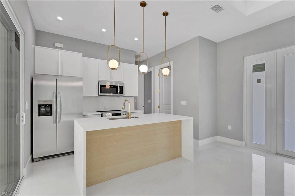 160 Logan Boulevard South Naples, FL 34119 - Photo 35 of 49 Kitchen featuring appliances with stainless steel finishes, pendant lighting, light stone countertops, white cabinets, and backsplash