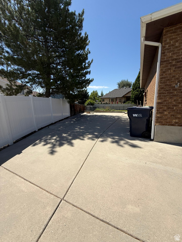 328 Heather Ridge Circle Sandy, UT 84070 - Photo 21 of 32 Expansive concrete driveway alongside a brick exterior, featuring a white vinyl fence and a mature tree providing natural shade
