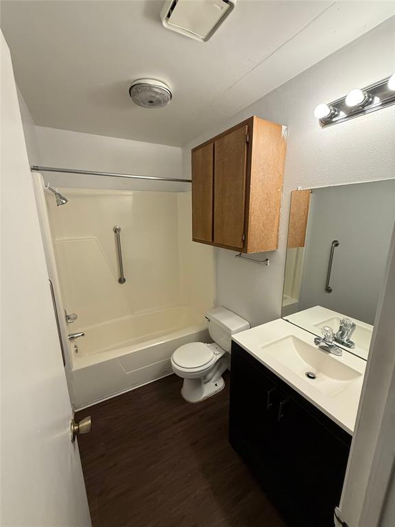 1708 Short Street, Unit B Cleburne, TX 76033 - Photo 5 of 8 Bathroom featuring a shower-tub combination with grab bars, wood-finish flooring, a toilet, a vanity with an integrated sink, and an overhead medicine cabinet