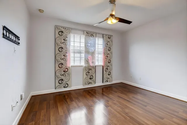 an empty room with wooden floor fan and windows
