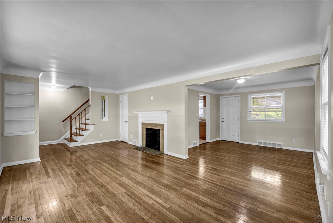 2313 North Taylor Road Cleveland Heights, OH 44112 - Photo 4 of 32 Spacious living area featuring polished wood-finish flooring, a classic fireplace with a stone surround and white mantel, a built-in bookshelf, and a staircase with wood railing