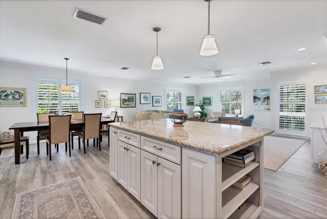 a kitchen with stainless steel appliances granite countertop center island a stove a refrigerator a dining table and chairs with wooden floor