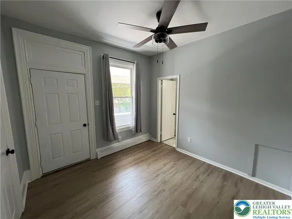 an empty room with wooden floor fan and windows