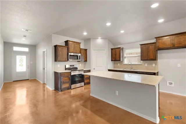 a kitchen with kitchen island granite countertop a sink a counter top space stainless steel appliances cabinets and a counter top space