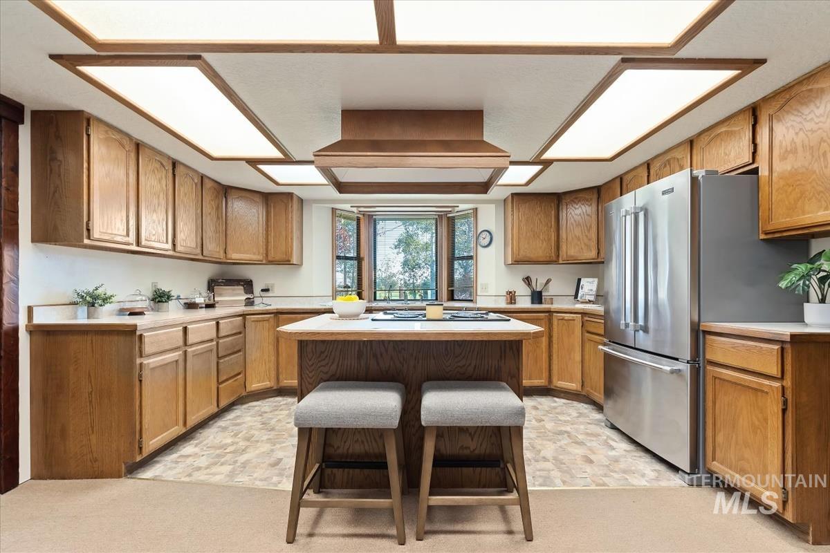 8275 Washoe Road Fruitland, ID 83619 - Photo 10 of 43 U-shaped kitchen with wood cabinetry, stainless steel refrigerator, center island with built-in cooktop, and bay window