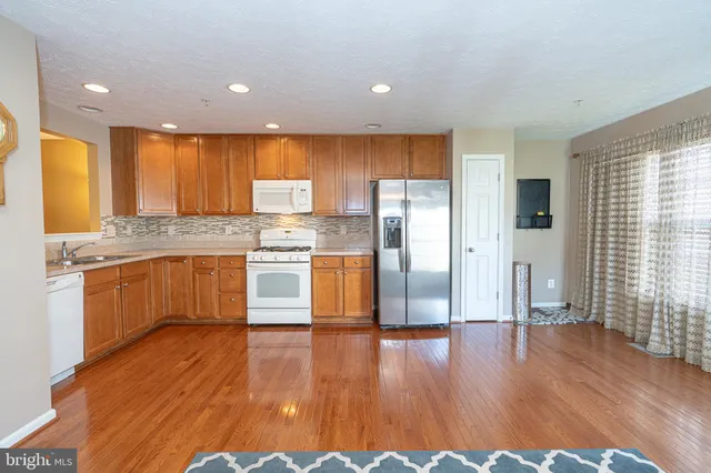 a kitchen with stainless steel appliances granite countertop a refrigerator a sink dishwasher a stove and white countertops with wooden floor