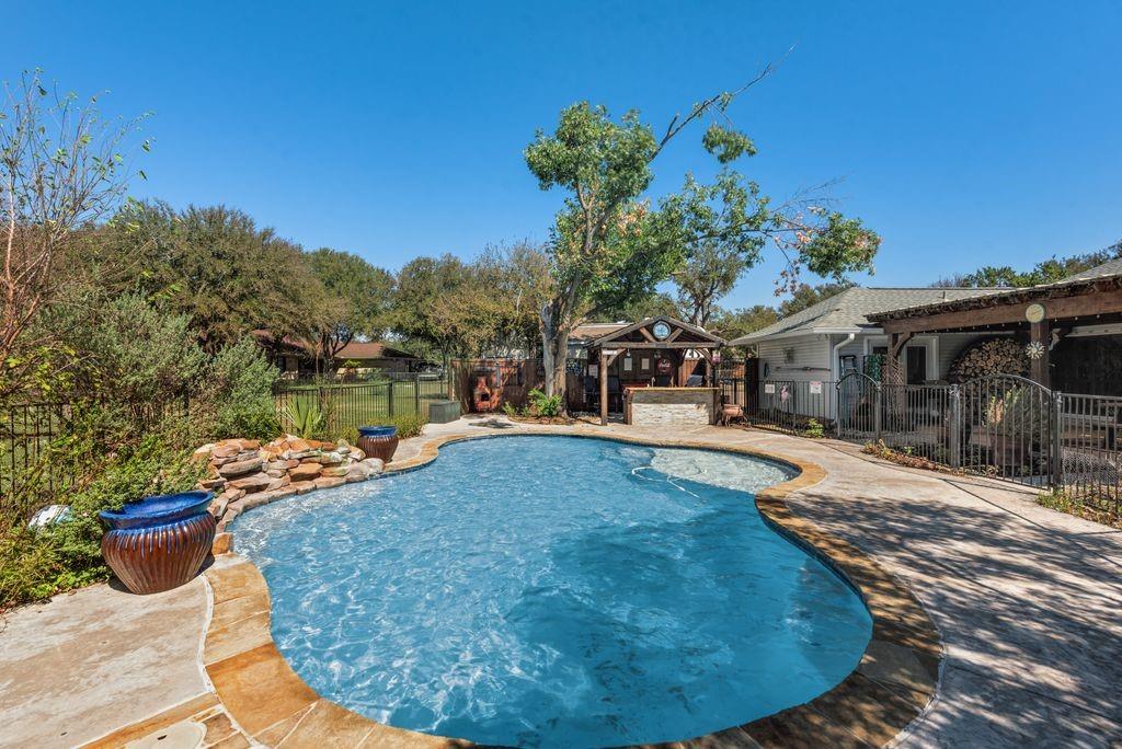 83 Crown Road Willow Park, TX 76087 - Photo 28 of 35 Freeform swimming pool with rock waterfall feature, stone coping, and a built-in poolside bar
