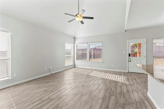 an empty room with wooden floor chandelier fan and windows