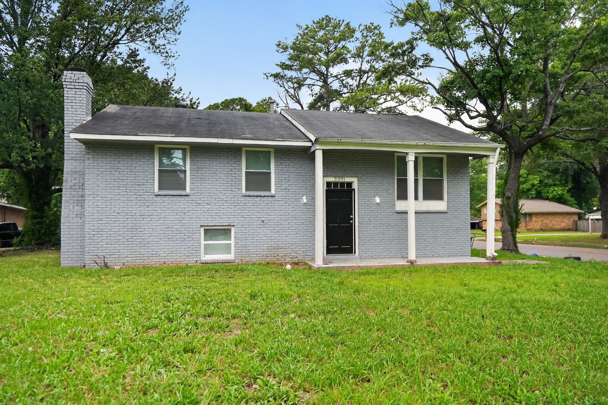 3391 South Perkins Road Memphis, TN 38118 - Photo 3 of 16 Gray brick exterior with a dark entry door, covered porch, multiple windows, and a prominent brick chimney