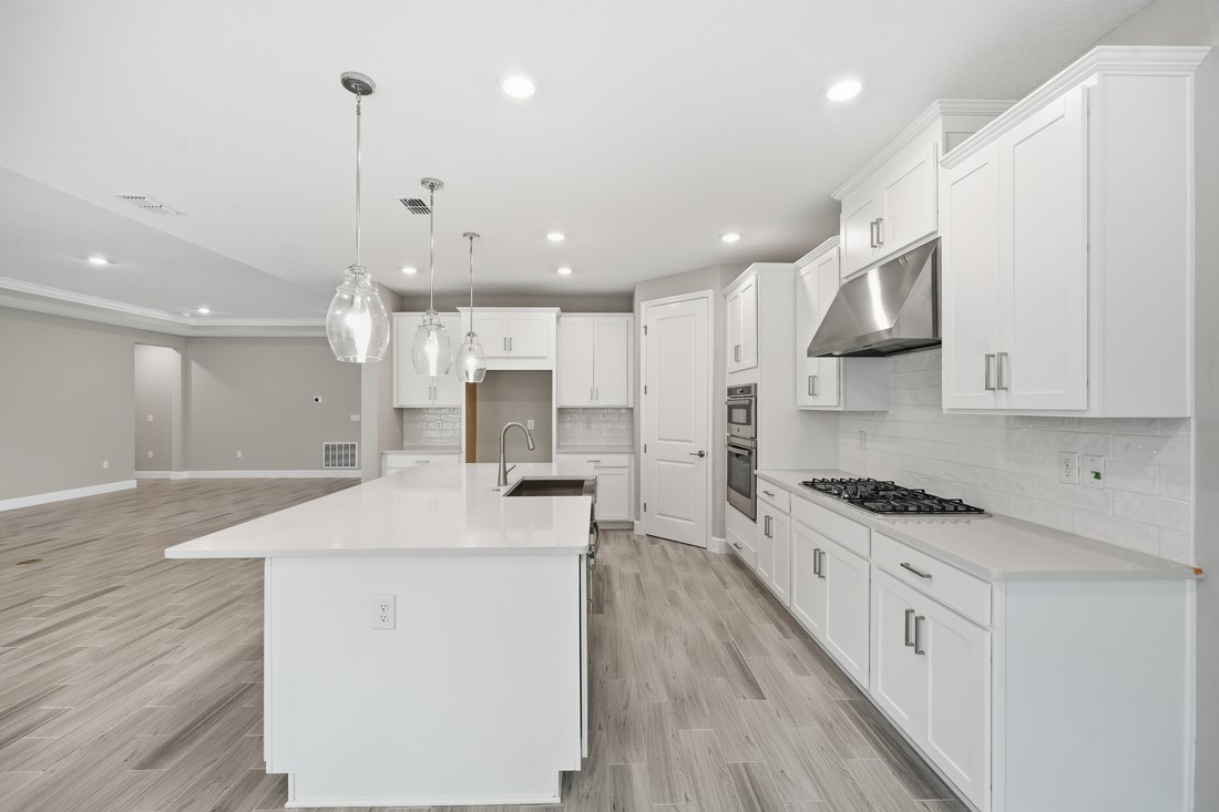 86049 Living Waters Run Yulee, FL 32097 - Photo 5 of 36 a kitchen with stainless steel appliances kitchen island granite countertop a stove a sink a refrigerator and white cabinets with wooden floor