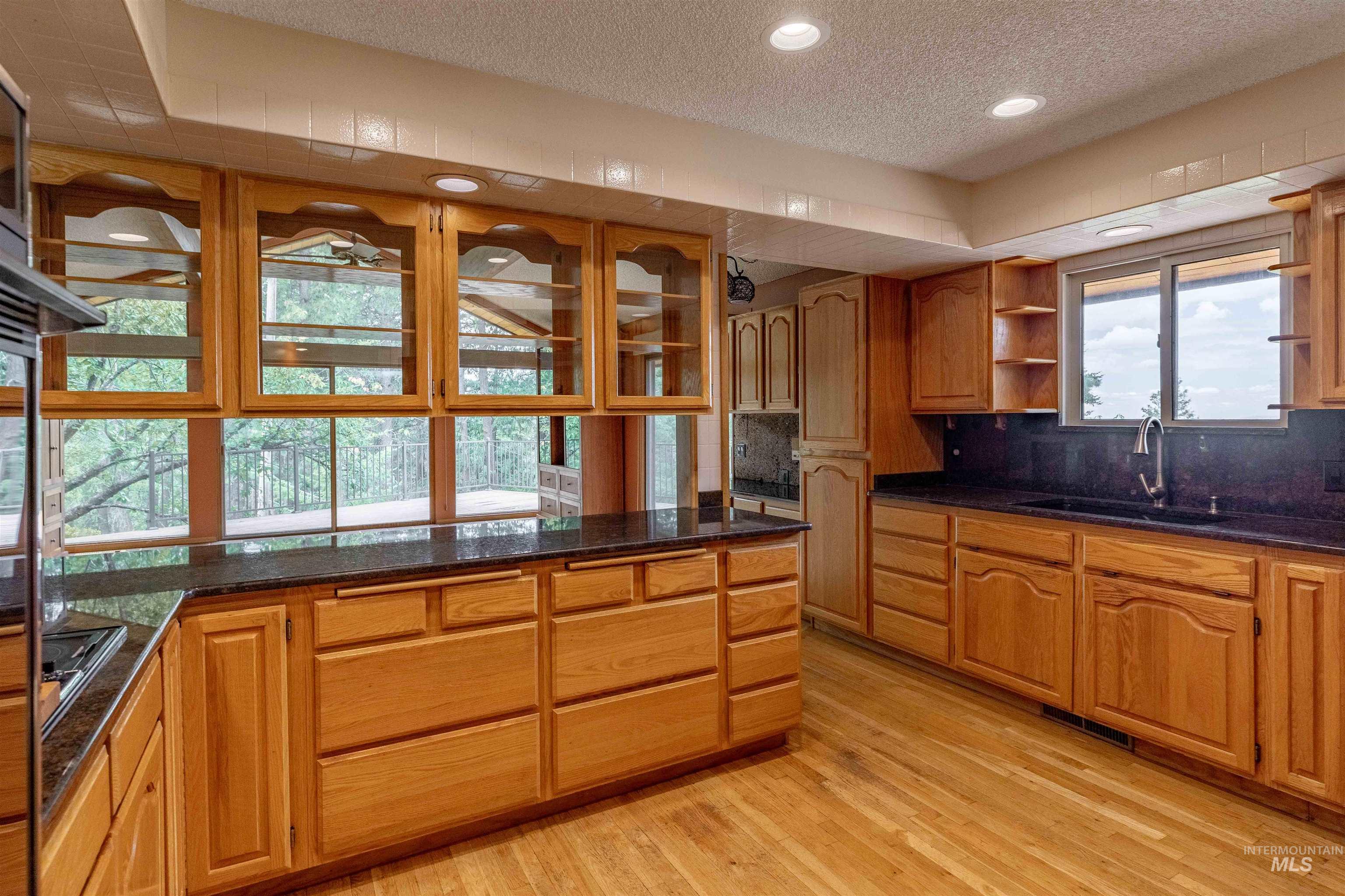 1050 Paradise Ridge Road Moscow, ID 83843 - Photo 10 of 49 Kitchen featuring wood finish cabinetry, decorative backsplash, light wood-style flooring, a textured ceiling, and dark stone countertops