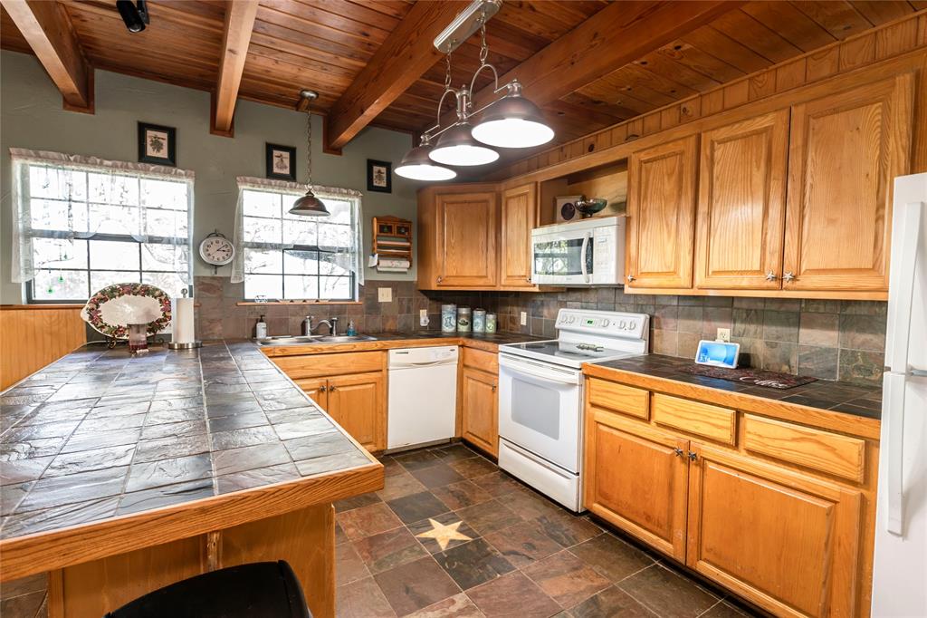 698 Storey Road Nocona, TX 76255 - Photo 25 of 34 Kitchen featuring white appliances, a wood ceiling with exposed beams, pendant lighting, brown cabinets, and tasteful backsplash