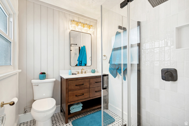 4883 South Center Street Murray, UT 84107 - Photo 18 of 32 Master/ Primary Bathroom. Bathroom featuring a freestanding wood-finish vanity with a white countertop and gold-tone faucet, a walk-in shower with a glass enclosure and matte black fixtures, shiplap accent wall, and mosaic tile flooring