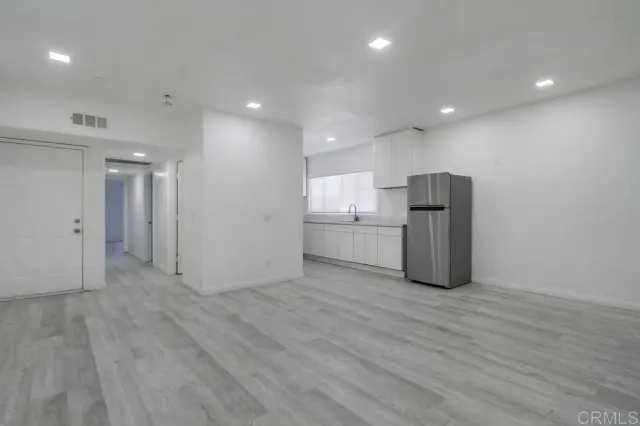 a view of an empty room with wooden floor and a kitchen