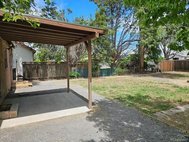 a view of a patio with a table and chairs under an umbrella with a small yard