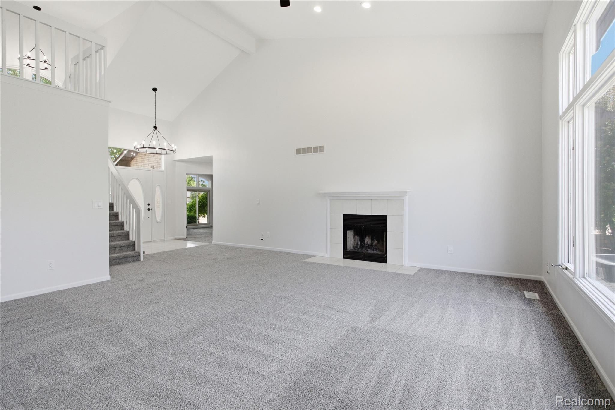 52658 Stag Ridge Drive Macomb, MI 48042 - Photo 6 of 28 Vaulted ceilings crown this living space, featuring a fireplace with a white mantel and tile surround, large windows, and gray patterned carpeting