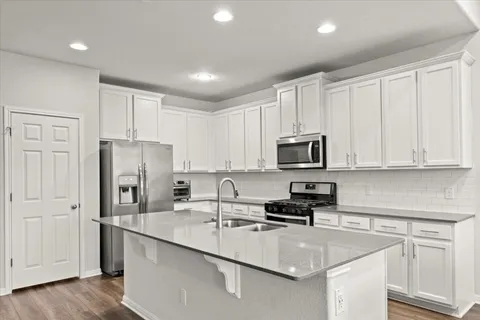 a kitchen with stainless steel appliances granite countertop a refrigerator a stove top oven a sink dishwasher a dining table and chairs with wooden floors