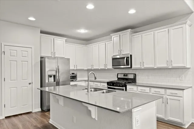 a kitchen with stainless steel appliances granite countertop a refrigerator a stove top oven a sink dishwasher a dining table and chairs with wooden floors