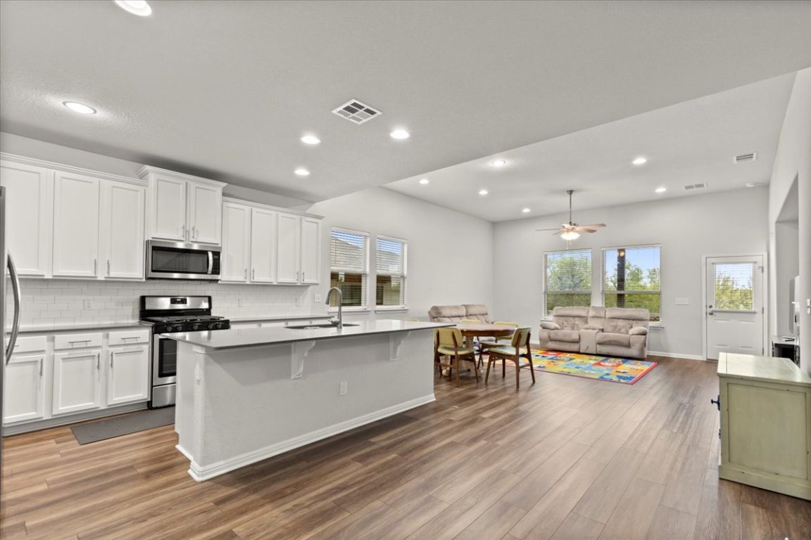 213 Munk Lane Leander, TX 78641 - Photo 9 of 40 a kitchen with stainless steel appliances granite countertop a refrigerator a stove top oven a sink dishwasher a dining table and chairs with wooden floors