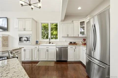 a kitchen with stainless steel appliances granite countertop a refrigerator a stove a sink and white cabinets with wooden floor