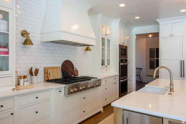 630 East Center Street Alpine, UT 84004 - Photo 22 of 115 Gourmet kitchen featuring a professional-grade stainless steel range, custom white range hood, white subway tile backsplash, built-in double oven, and a large island with an undermount sink and brass faucet