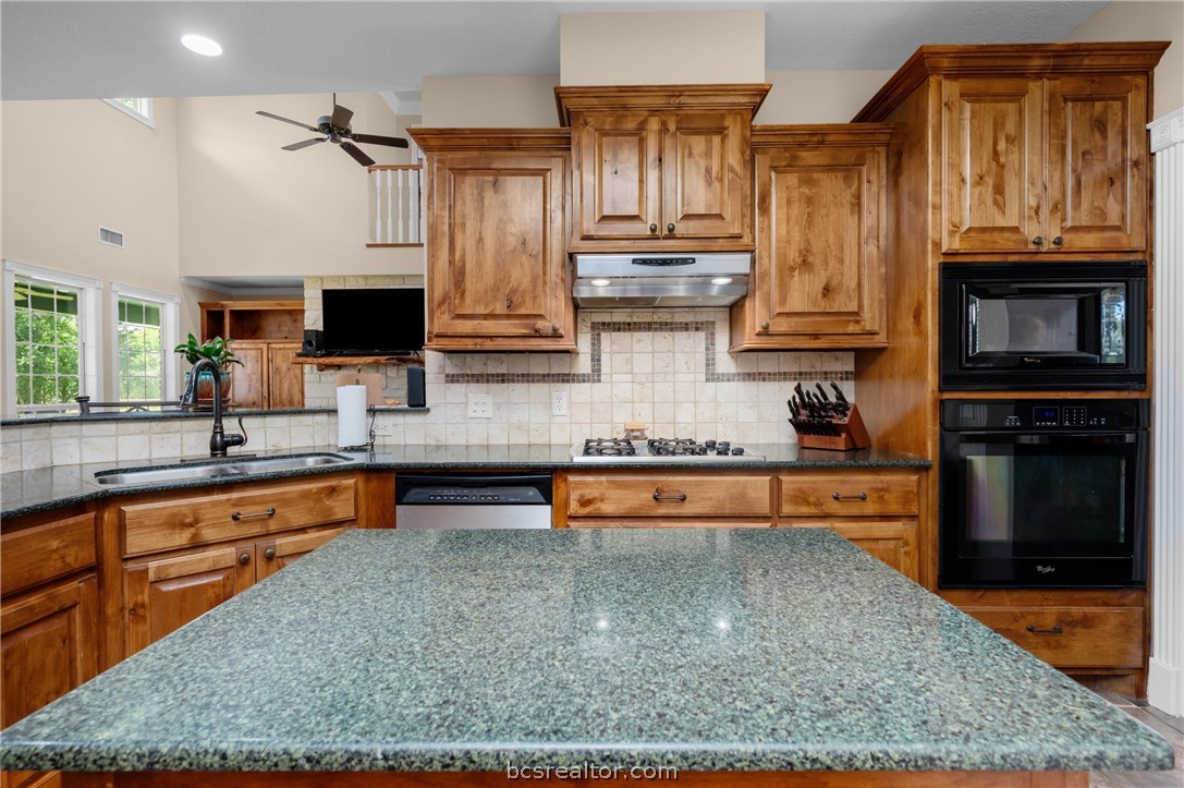 6400 Koppe Bridge Road College Station, TX 77845 - Photo 22 of 47 Kitchen featuring dark granite counters, black appliances, and custom wood finish cabinetry.