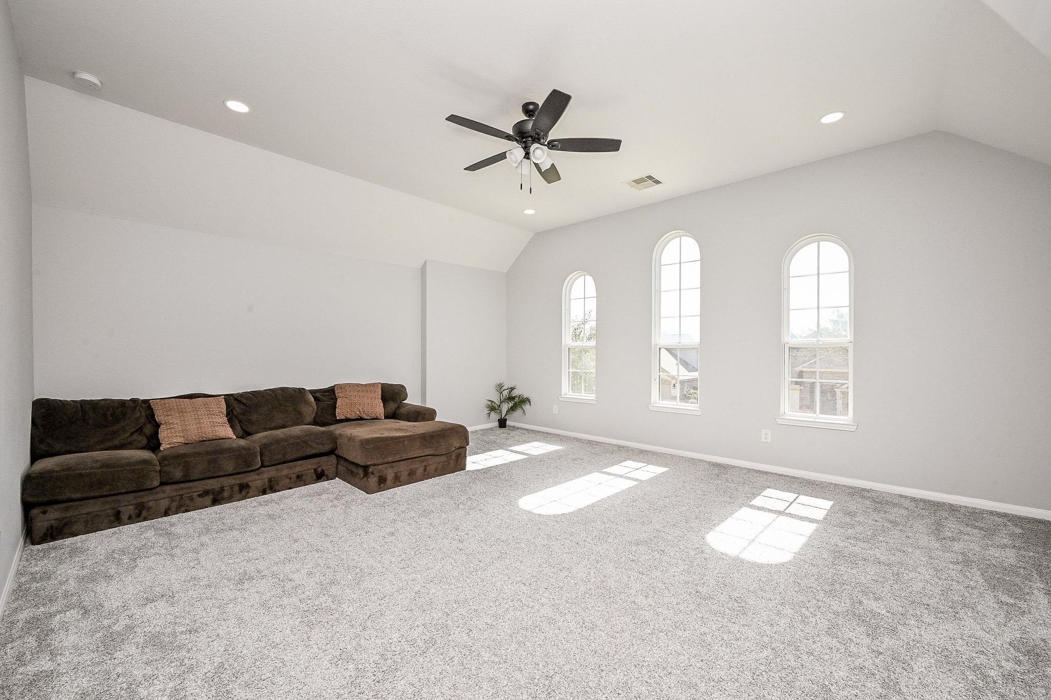 7042 Sliding Rock Circle Spring, TX 77379 - Photo 31 of 44 Spacious and bright game room featuring plush carpeting, elegant arched windows, and a cozy sectional sofa—perfect for relaxation and entertainment.