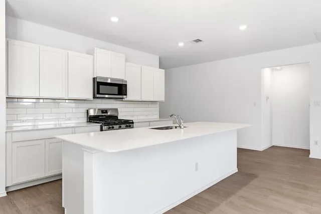 a kitchen with stainless steel appliances a sink a stove a microwave a sink a refrigerator white cabinets and wooden floor