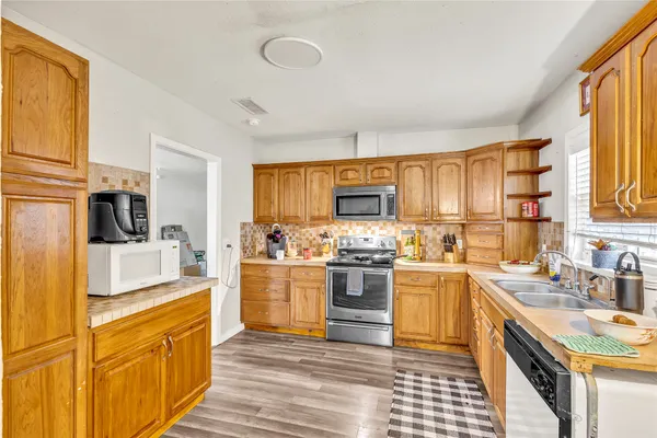a kitchen with stainless steel appliances granite countertop a stove top oven a sink dishwasher and a refrigerator with wooden cabinets