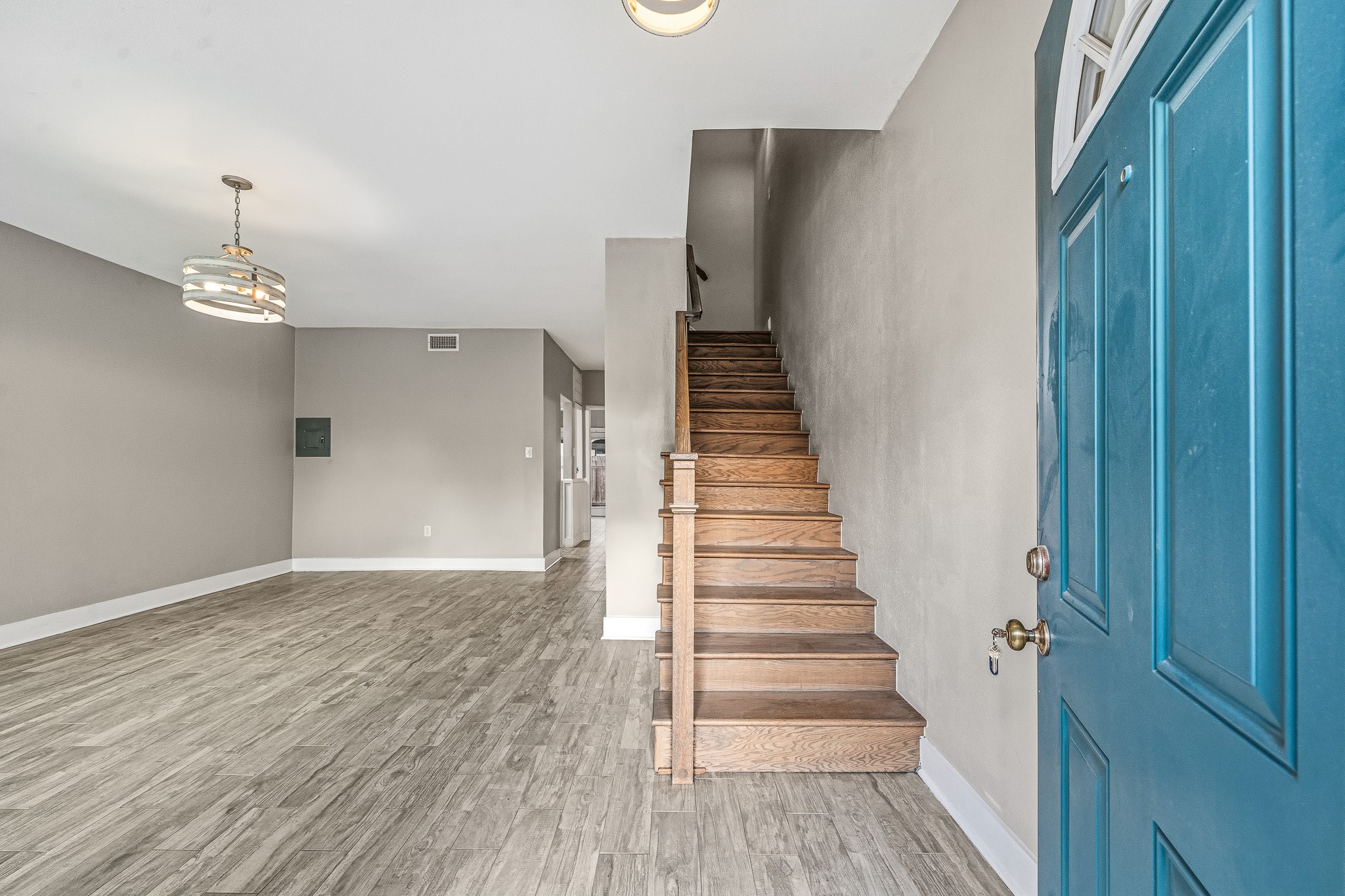 830 Threadneedle Street, Unit 240 Houston, TX 77079 - Photo 4 of 33 This photo showcases a modern entryway with sleek wood flooring and neutral-toned walls. The open space features a stylish light fixture, a staircase leading upwards, and a bright blue door, creating a welcoming and contemporary atmosphere.
